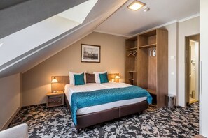 Un dormitorio con techo inclinado, una cama con manta azul, dos lámparas de noche y un cuadro en la pared.