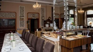 A formal dining room with a long table, cushioned seating, a buffet station, and chandeliers. - Erzsébet Királyné Szálloda (Godollo)