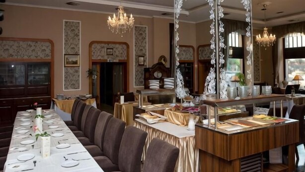 A formal dining room with a long table, cushioned seating, a buffet station, and chandeliers. - Erzsébet Királyné Szálloda (Godollo)
