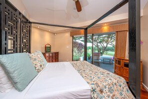 A bedroom with a large bed, a wooden dresser, a chair, and a view of the outdoors.