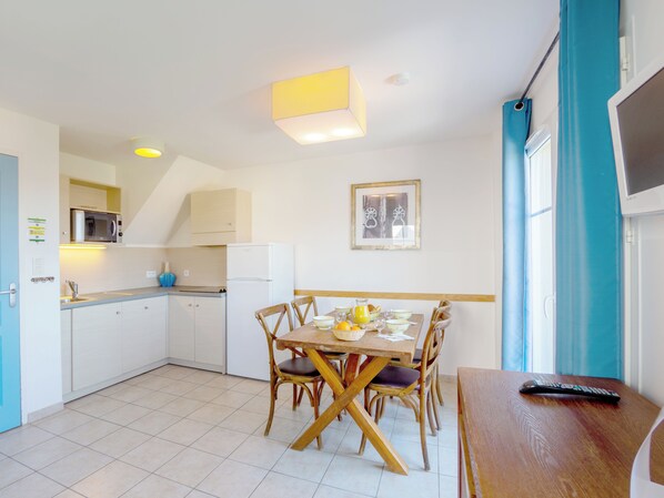 A compact kitchen with a dining area, a microwave, a refrigerator, and a table set for two.