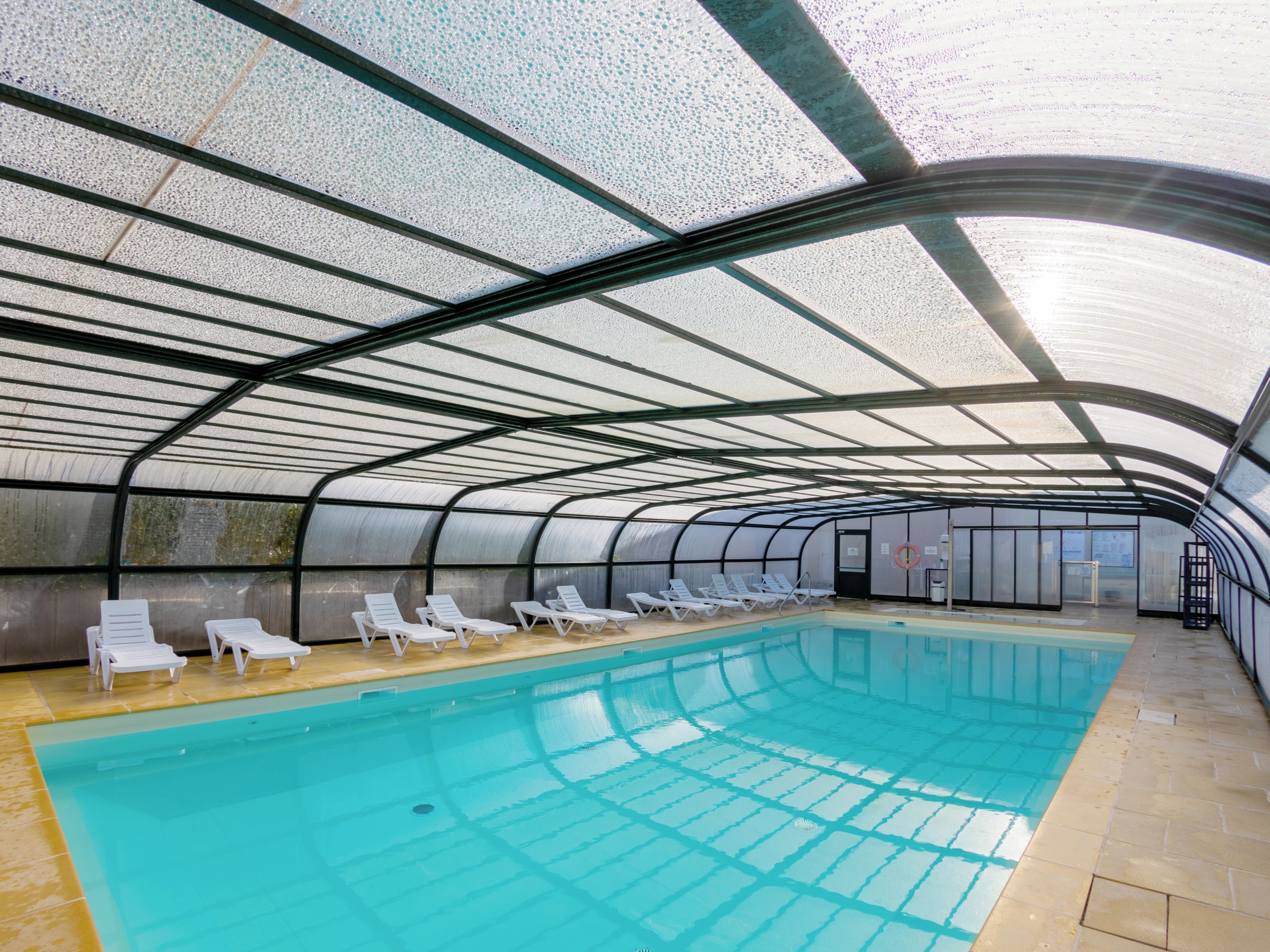 Una piscina interior con techo curvo y varias sillas de descanso a lo largo de los bordes.