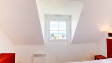 A room with a sloped ceiling, a window with a view, a bed, a bedside table, and a red dresser.