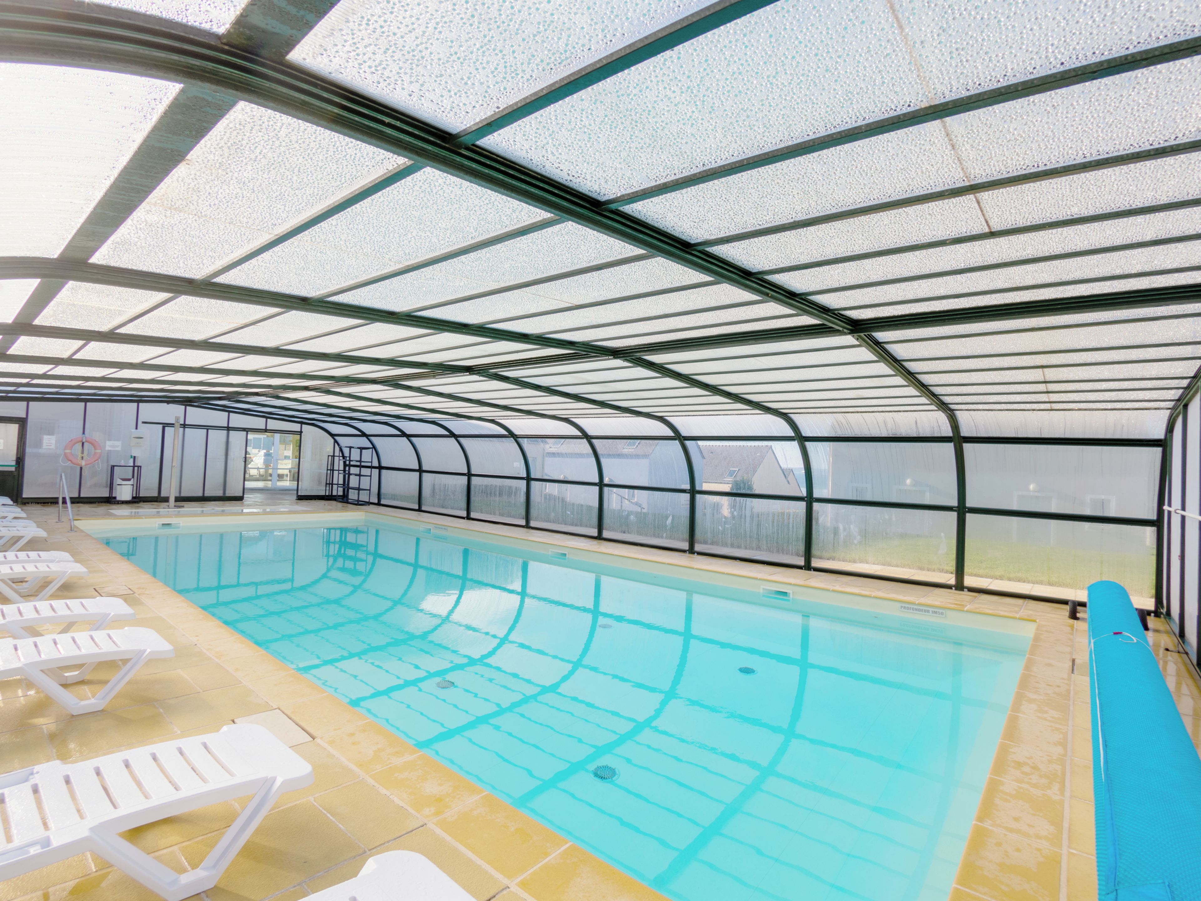 An indoor swimming pool with clear lanes, a lifeguard stand, and lounge chairs along the side.