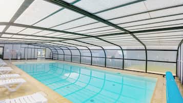 Ein Hallenbad mit deutlichen Bahnen, einem Rettungsschwimmerstand und Liegestühlen am Rand.