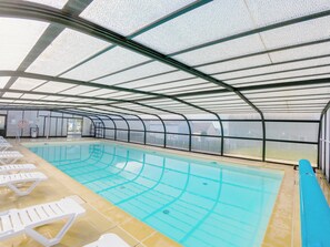 An indoor swimming pool with clear lanes, a lifeguard stand, and lounge chairs along the side.