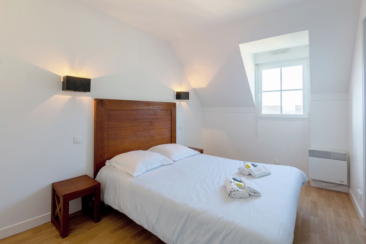 Un dormitorio con cabecera de madera, una mesita de noche pequeña, una ventana y aire acondicionado instalado en la pared.