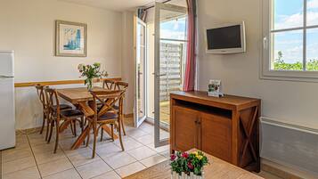 Un comedor con mesa y sillas de madera, un mueble de madera pequeño, un televisor montado en la pared y una ventana con vistas a zonas verdes.