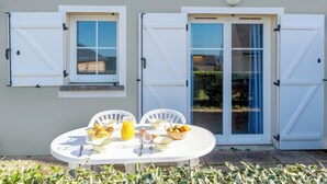 A dining table set outdoors with a view of a house, featuring a window, a door, and a small balcony. - Residence Vacanceole Les Terrasses De Pentrez (Saint-Nic)