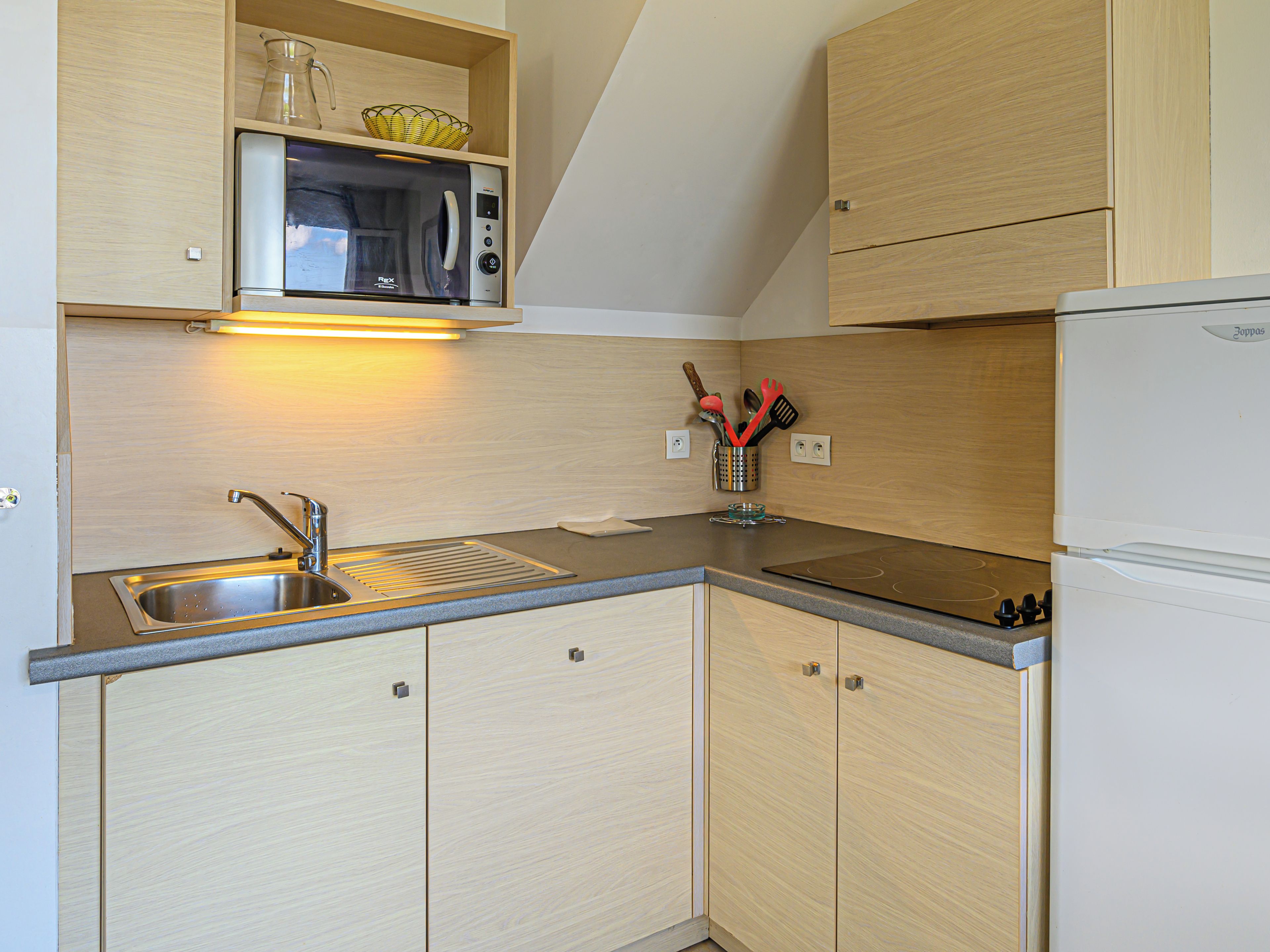 A compact kitchen with a built-in microwave, a stainless steel sink, and wooden cabinets.