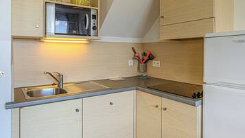 A compact kitchen with a built-in microwave, a stainless steel sink, and wooden cabinets.