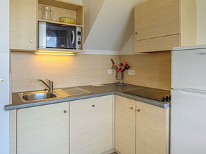 Cocina compacta con microondas integrado, un lavamanos de acero inoxidable y armarios de madera.