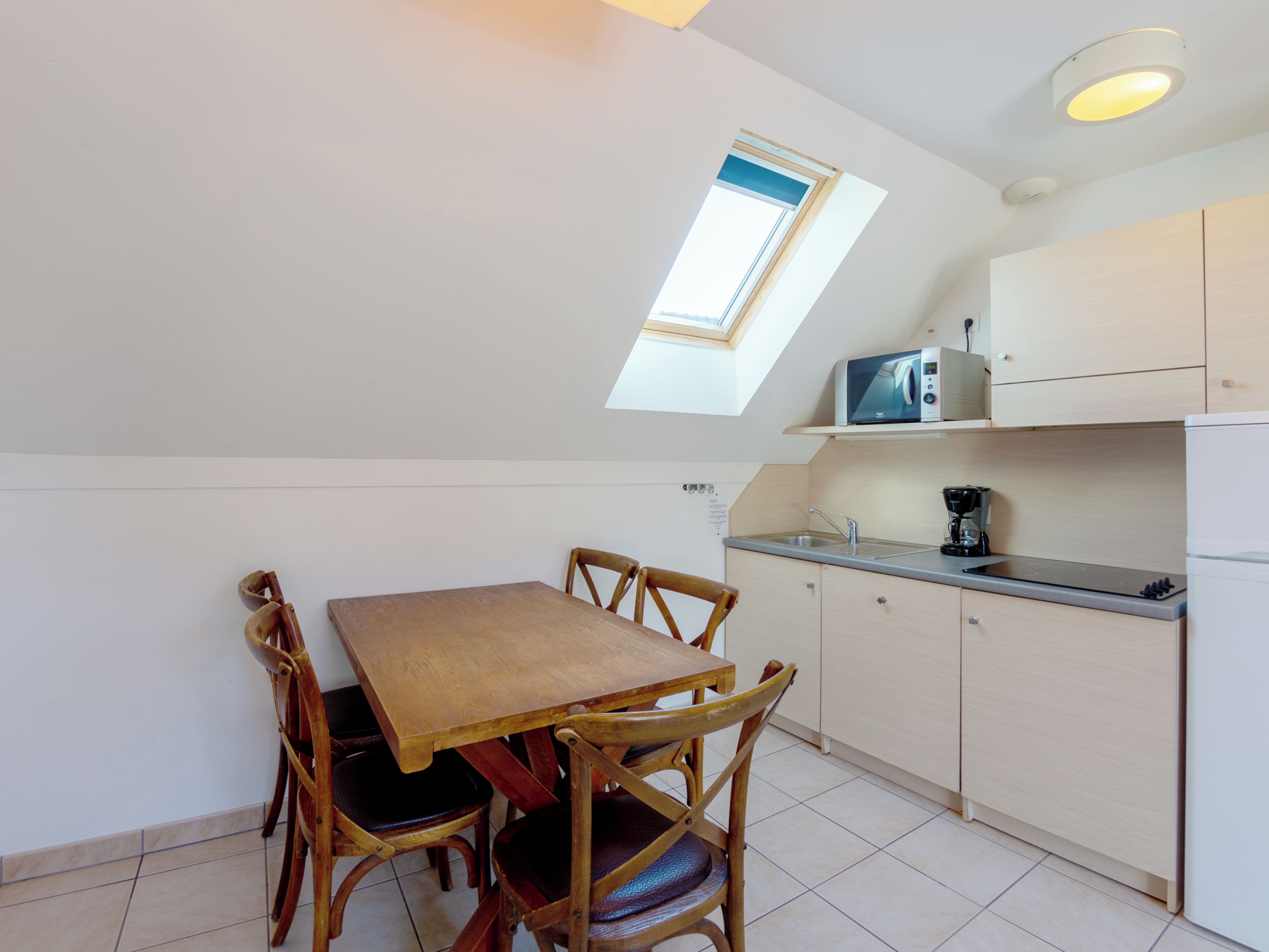 A compact kitchen with a dining table and chairs, a built-in microwave, and a small window.