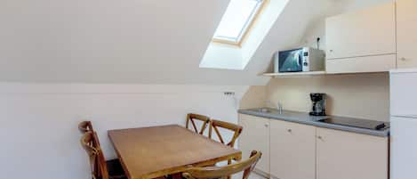 A compact kitchen with a dining table and chairs, a built-in microwave, and a small window.