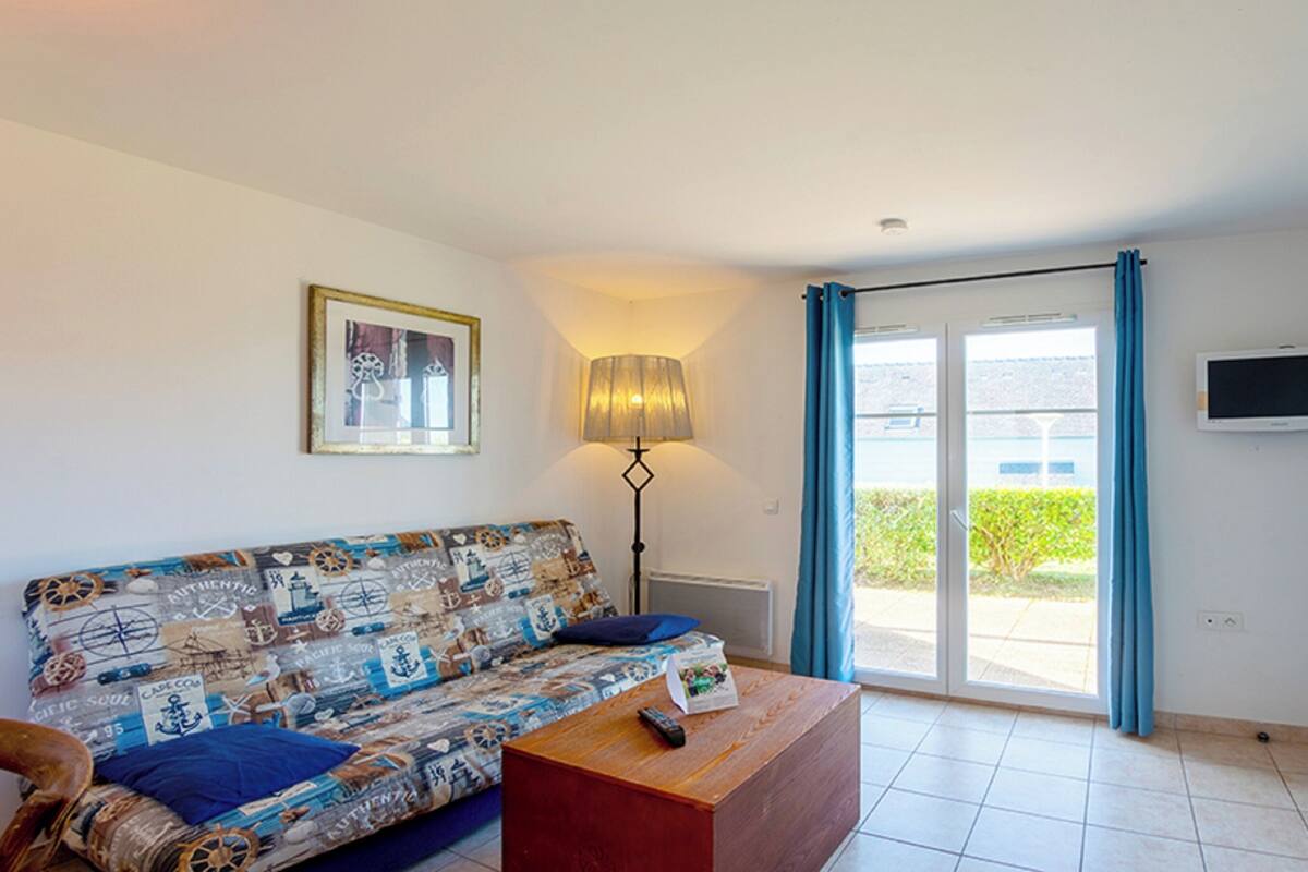 Ein Wohnzimmer mit einem gemusterten Sofa, einem Couchtisch, einer Stehlampe, einem Fernseher und einer Schiebetür zum Außenbereich.