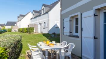 Propiedad residencial con patio amoblado, que incluye mesa y sillas, una puerta blanca y césped cuidado.