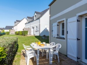 Propiedad residencial con patio amoblado, que incluye mesa y sillas, una puerta blanca y césped cuidado.
