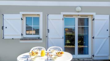 A dining table set outdoors with a view of a house, featuring a window, a door, and a small balcony.
