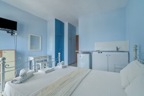 Een hotelkamer met een bed, een bureau, een spiegel, een televisie en een kitchenette.