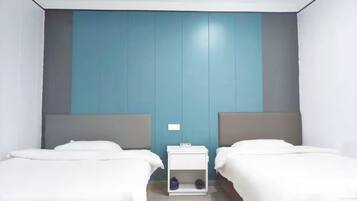 A hotel room with two beds, a small bedside table, and a wall with a blue panel.