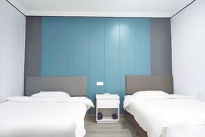 Una habitación de hotel con dos camas, una mesita de noche pequeña y una pared con un panel azul.