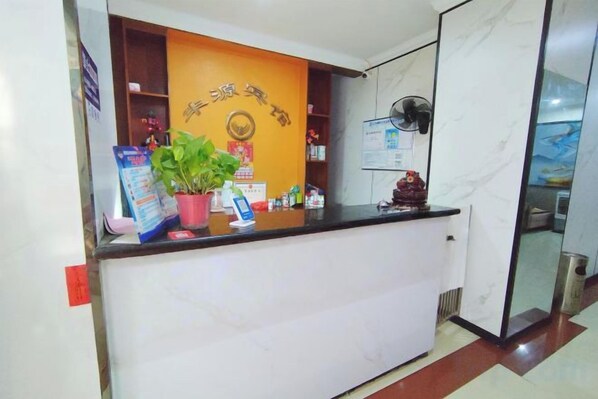 A reception desk with a potted plant, a wall-mounted fan, and a bulletin board. - Fengyuan Hotel (Hengyang Jiefang Road Shigu Academy) (Hengyang)