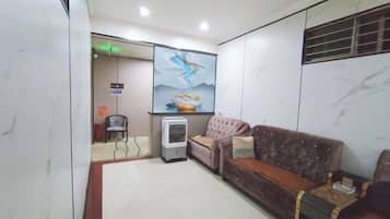 Zona de recepción con un sofá, una mesita, un televisor en la pared y una puerta que da a otra habitación.