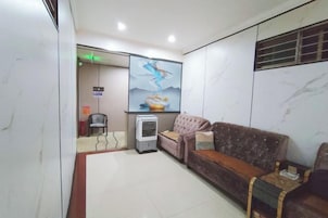 Zona de recepción con un sofá, una mesita, un televisor en la pared y una puerta que da a otra habitación.
