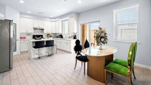 Une cuisine moderne avec des meubles blancs, un réfrigérateur en acier inoxydable et un îlot en marbre agrémenté de tabourets de bar.