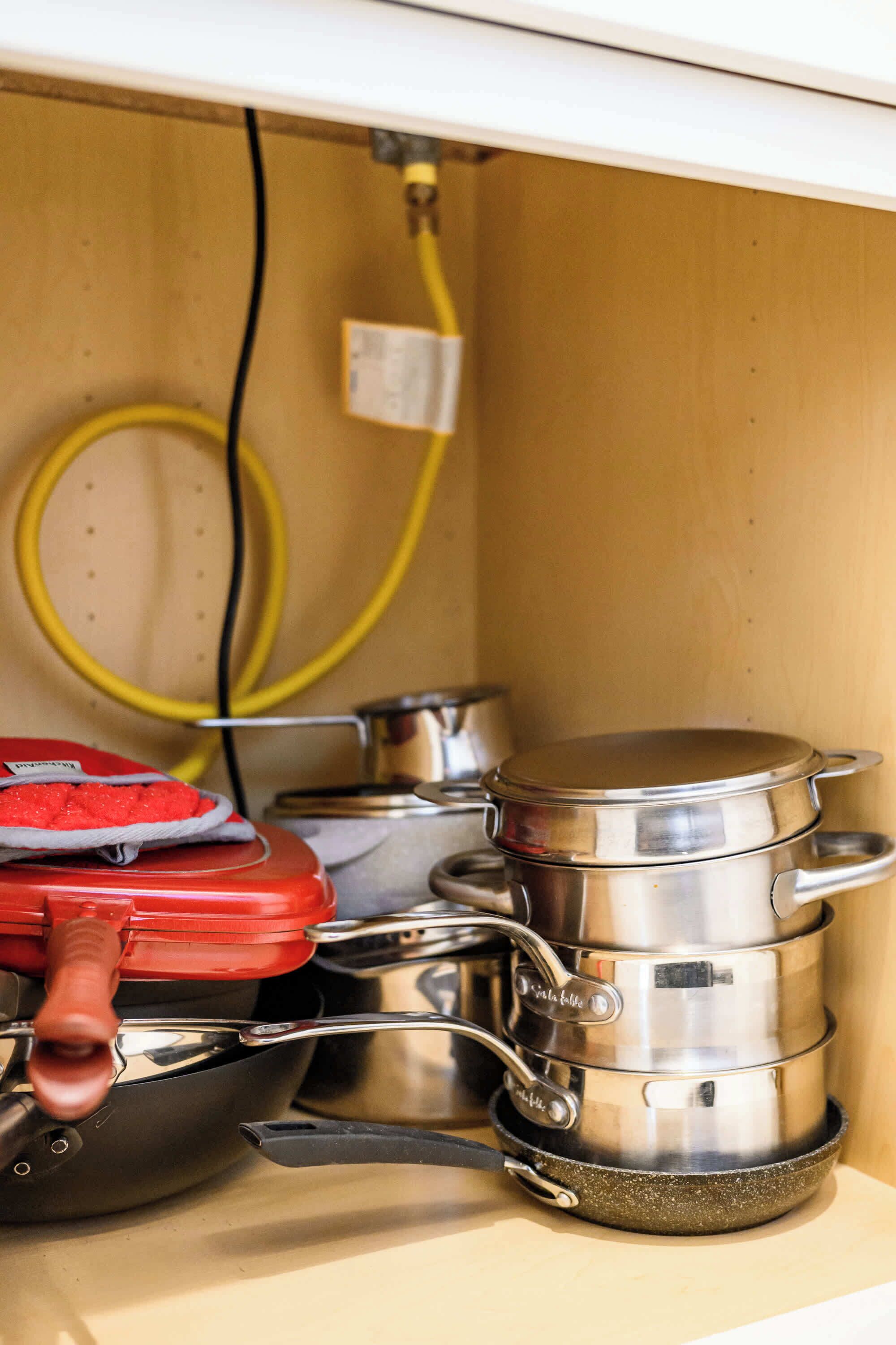 A kitchen with stainless steel cookware, including pots and pans, and a red appliance.