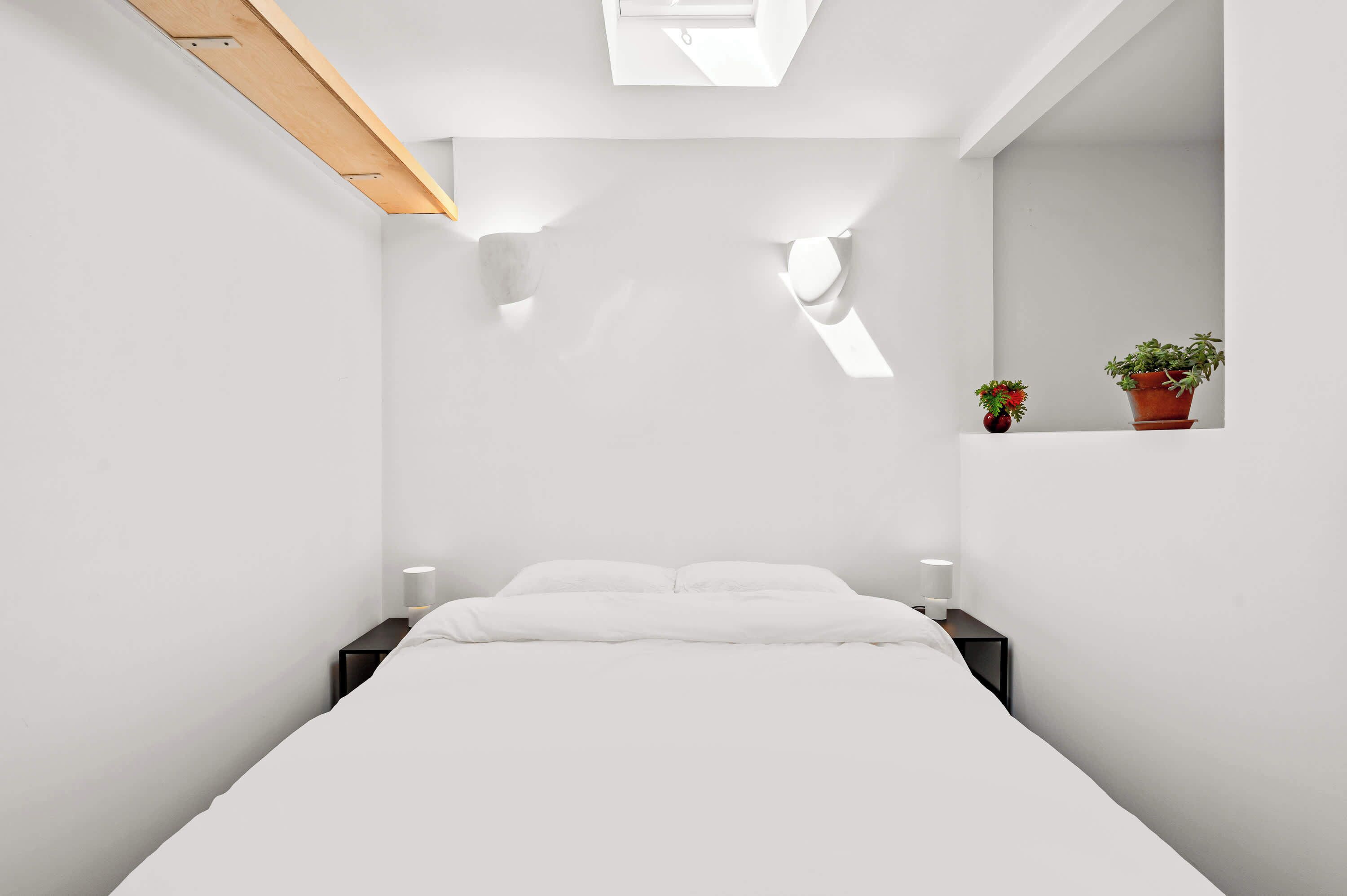 A minimalist bedroom with a bed, bedside tables, and a skylight.