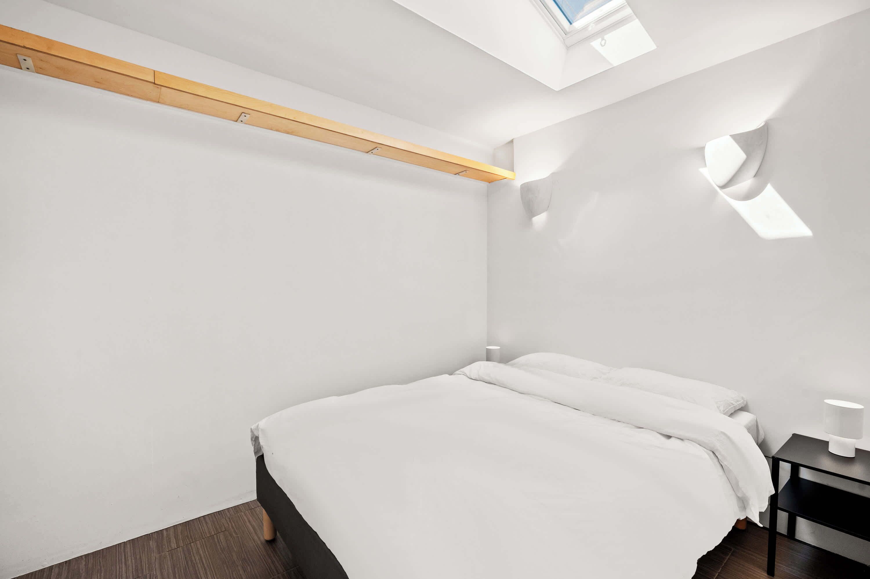 A minimalist bedroom with a bed, a nightstand, and a skylight.