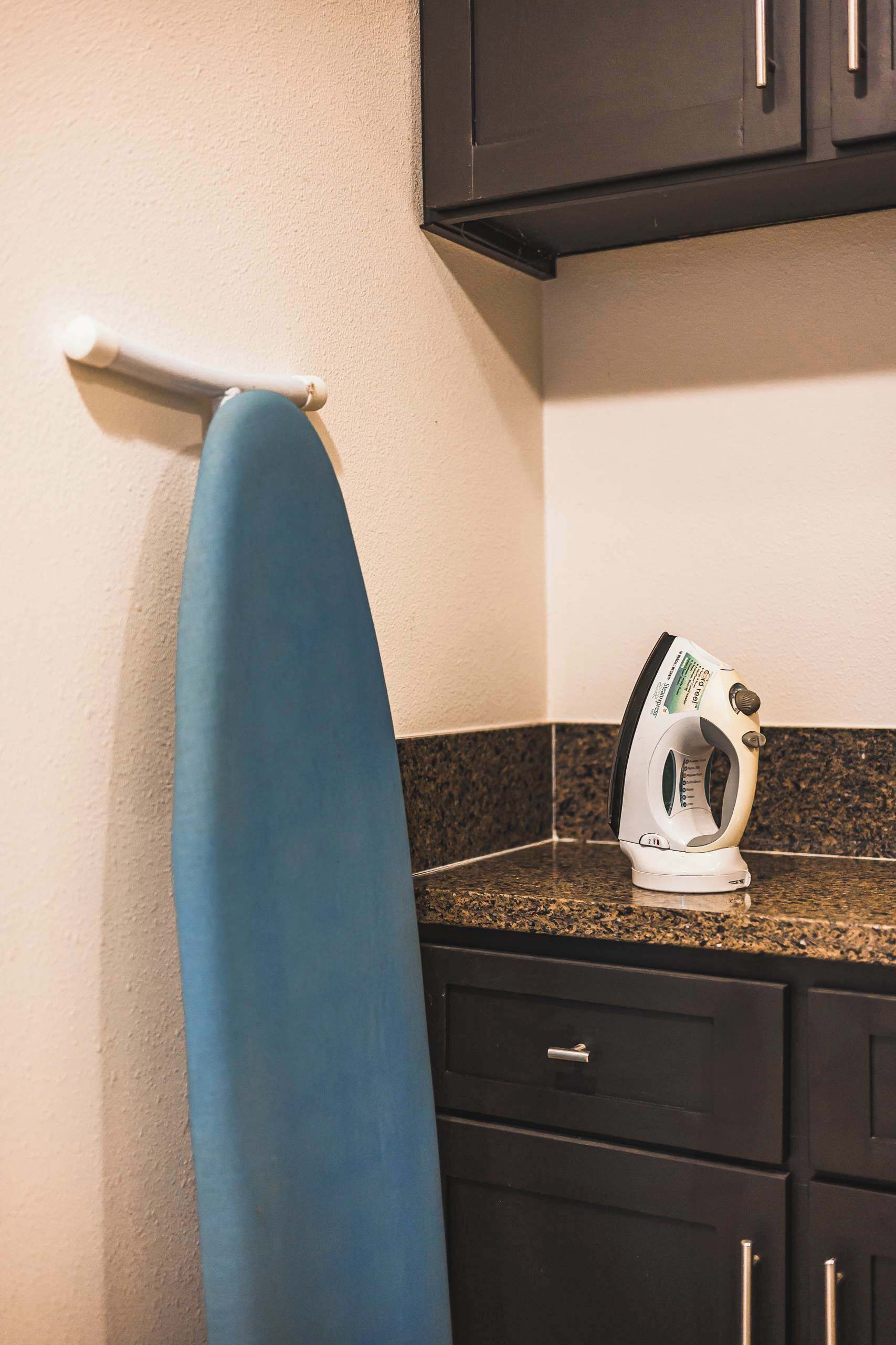 A kitchen with a countertop, an ironing board, and a white iron.