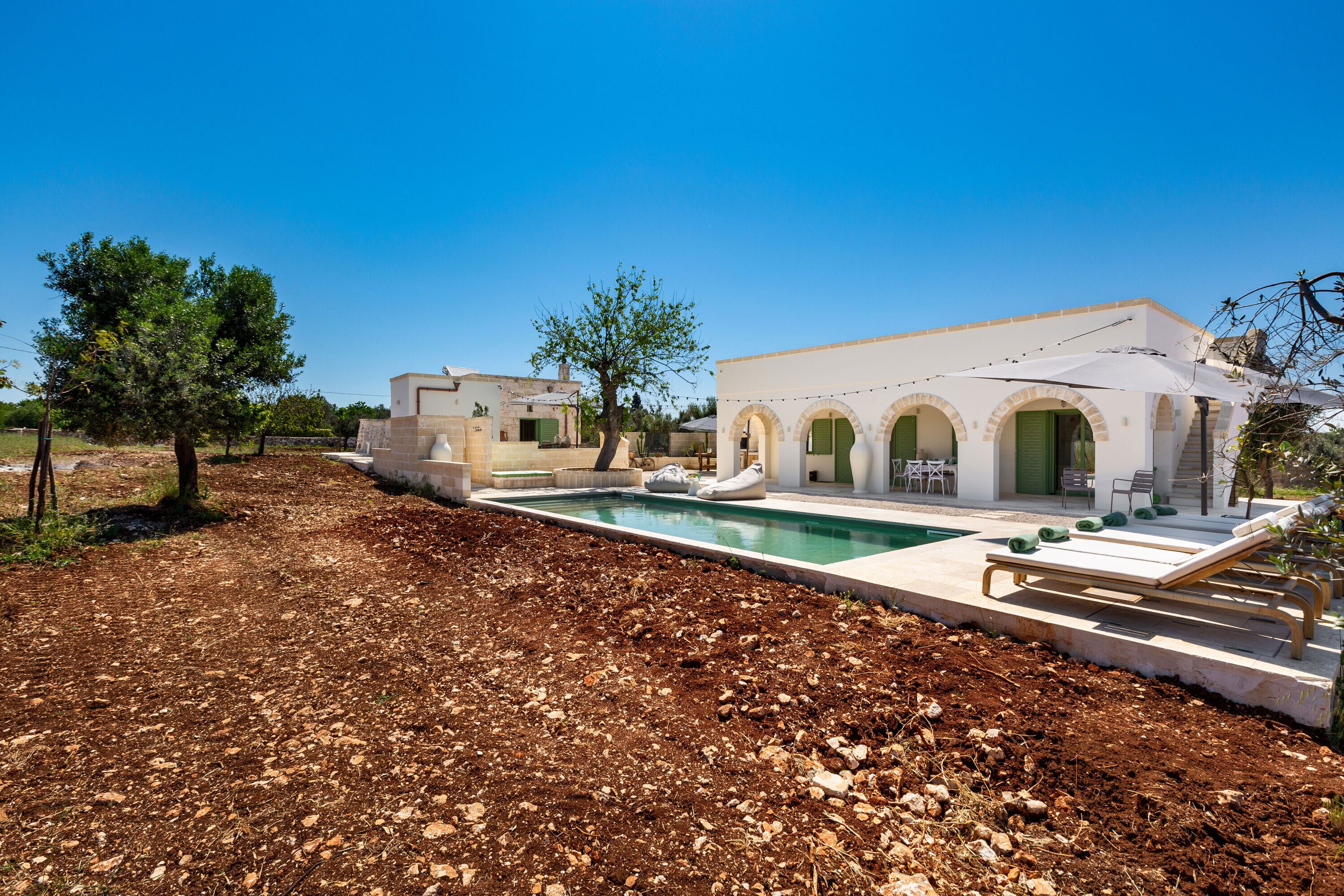Una villa moderna con piscina, mobiliario de exterior y un jardín ajardinado.