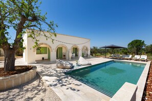 Ein Poolbereich mit klarem Pool, Liegestühlen und einem Gebäude mit Rundbogenfenstern.