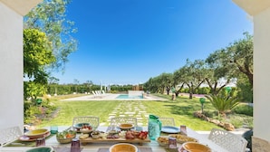 Un área de comedor al aire libre con vista a una piscina y jardín.