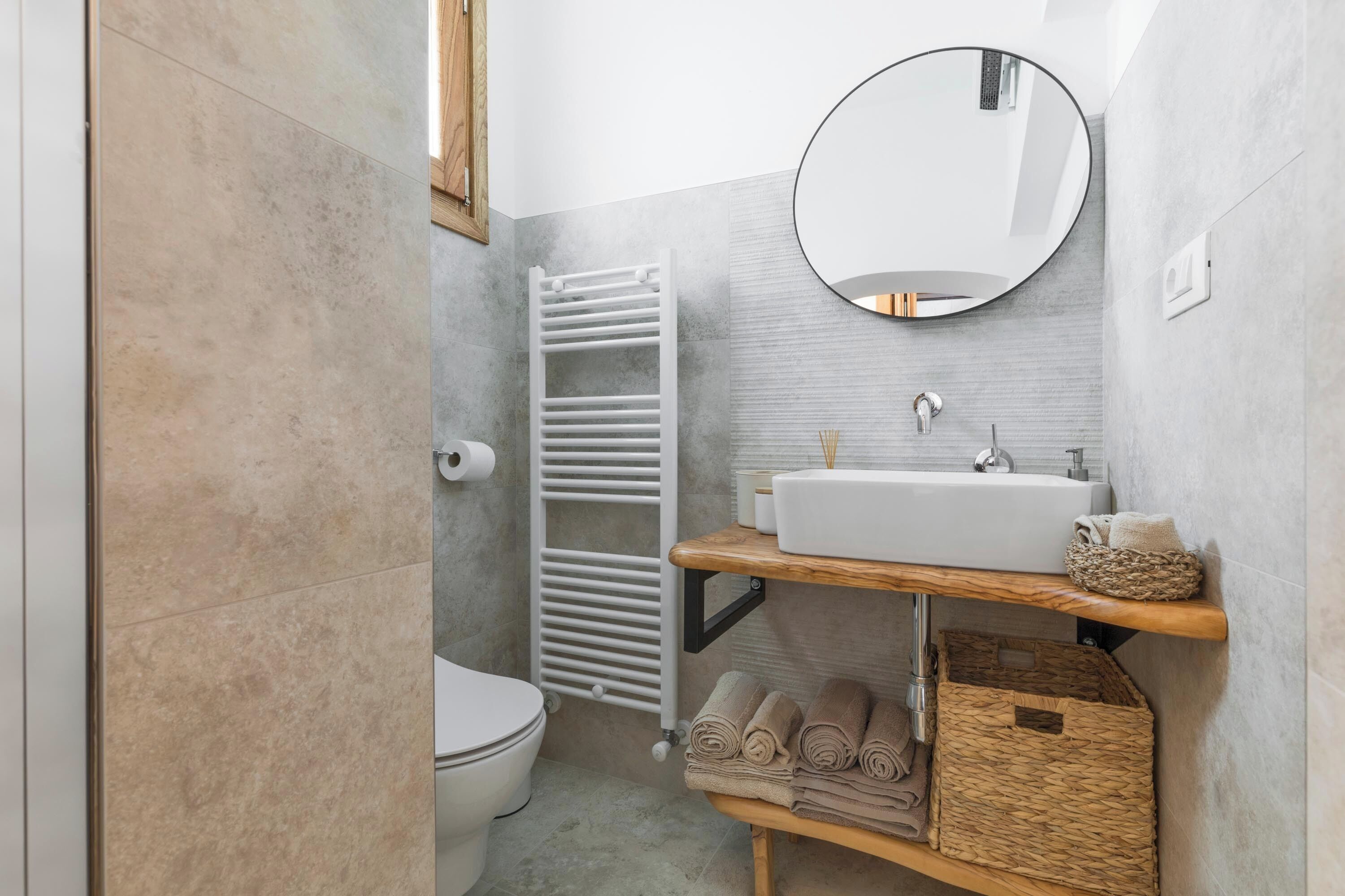 A modern bathroom with a white sink, round mirror, and tiled walls.