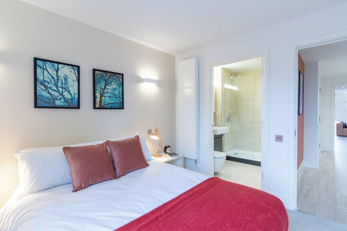 Un dormitorio moderno con una cama grande, una manta roja y dos obras de arte enmarcadas en la pared.