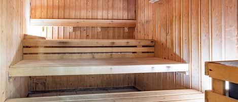 A wooden sauna with benches and a sloped floor.