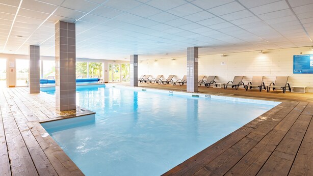 Una piscina interior con cubierta de madera, sillas de descanso y techo de azulejos.