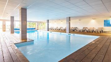 Une piscine intérieure dotée d’un pont en bois, de chaises longues et d’un plafond carrelé.