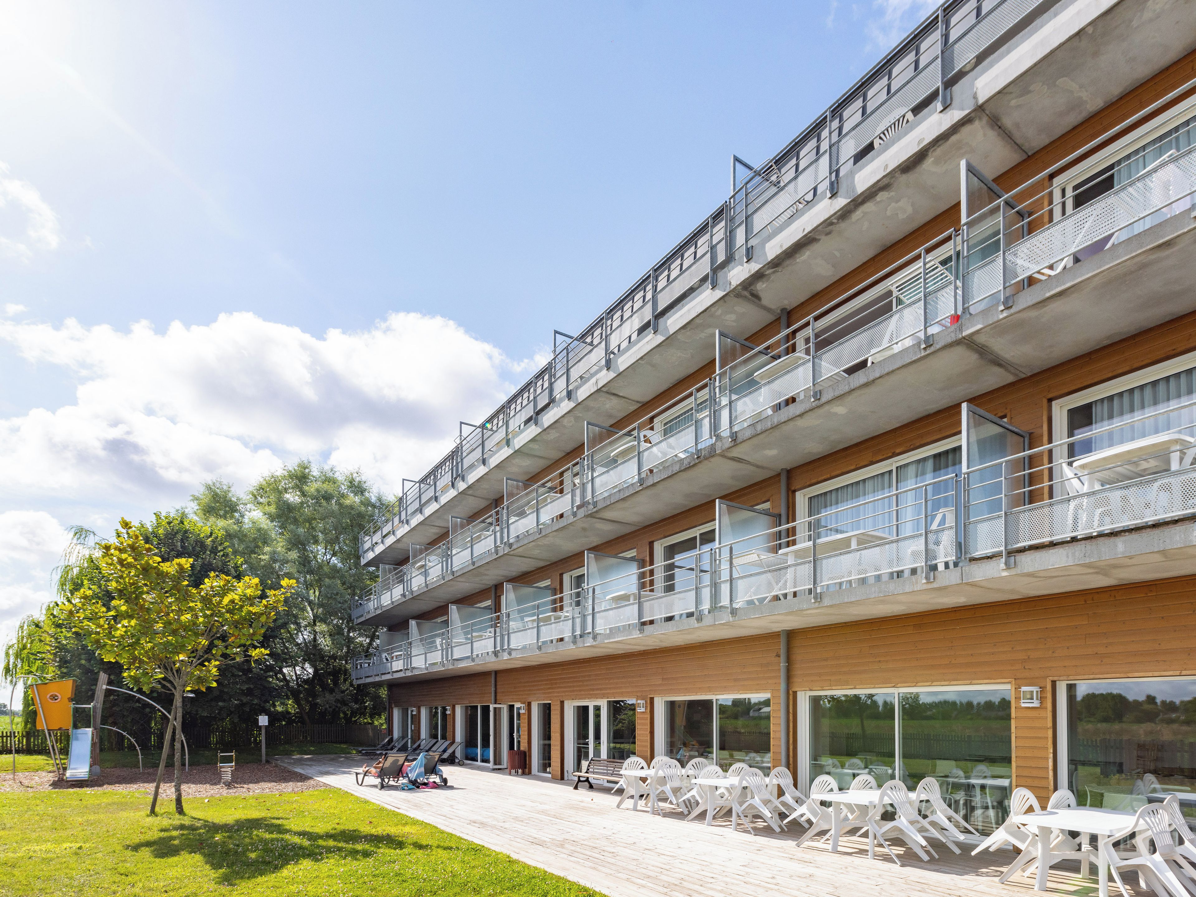 A multi-story building with balconies, outdoor seating, and a playground.