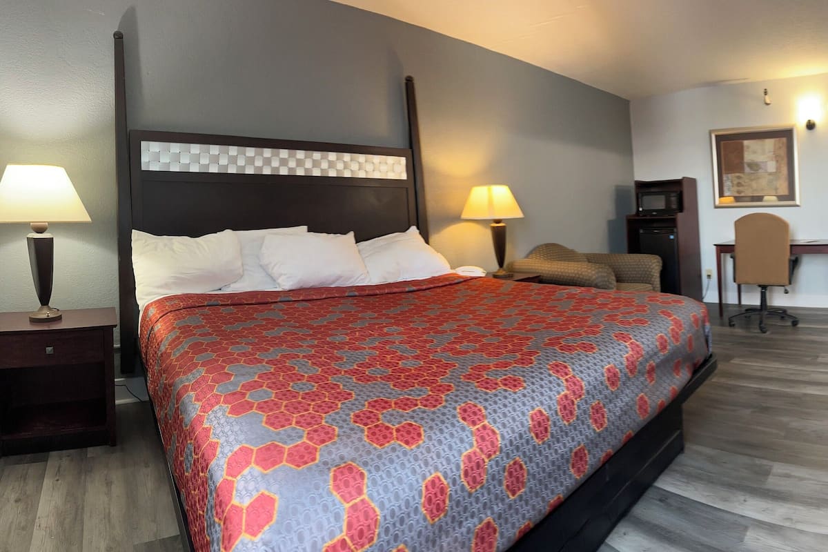 A hotel room with a large bed, a desk, a chair, a TV, and a door leading to another room.