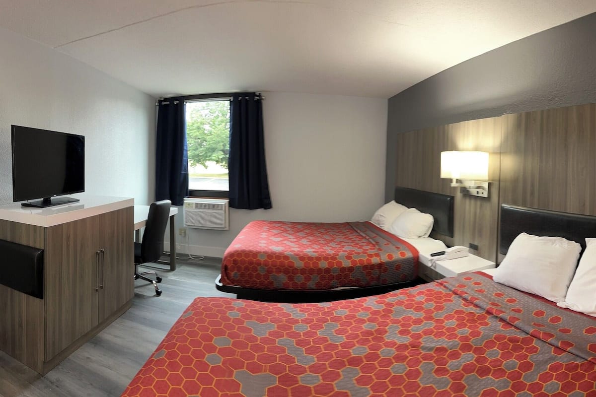 A hotel room with two beds, a desk, a TV, and a window with curtains.