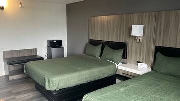 A hotel room with two beds, a bedside table, a nightstand, a lamp, and a wall-mounted light.