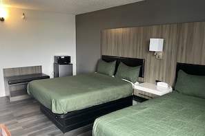 A hotel room with two beds, a bedside table, a nightstand, a lamp, and a wall-mounted light. - Coratel Inn and Suites By Jasper Roseville (Roseville)