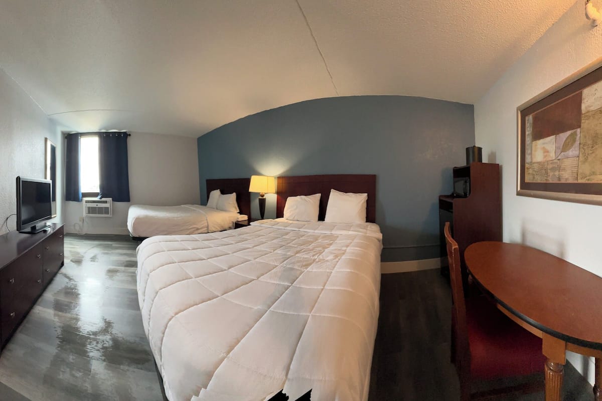 A hotel room with a large bed, a smaller bed, a desk, a TV, and a painting on the wall.