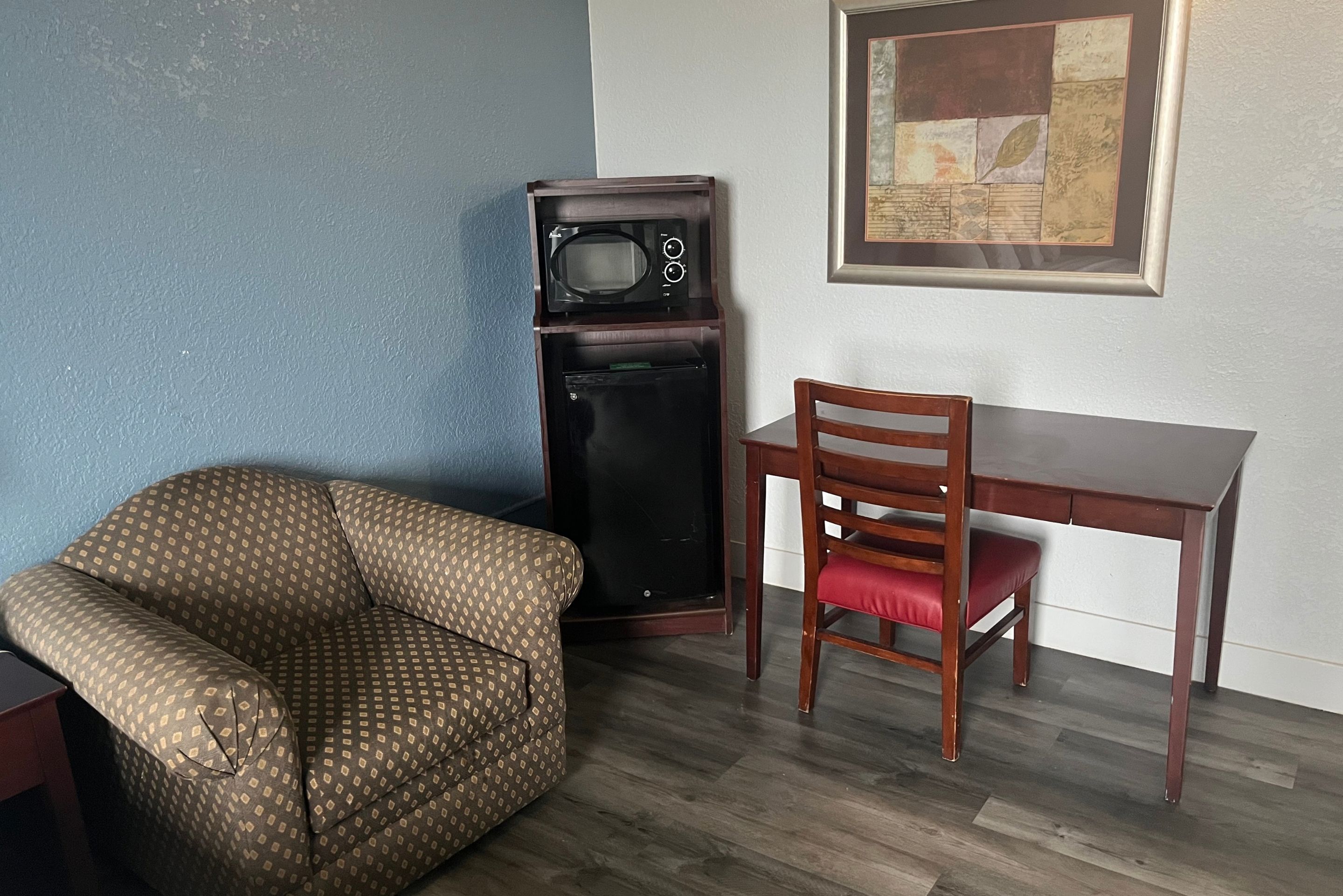 Una habitación con un sillón estampado, una mesa de comedor de madera, un refrigerador negro alto y una obra de arte enmarcada en la pared.
