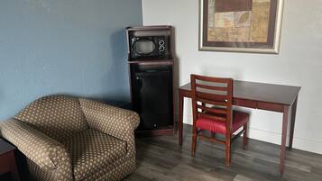 Una habitación con un sillón estampado, una mesa de comedor de madera, un refrigerador negro alto y una obra de arte enmarcada en la pared.