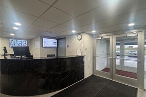 A reception area with a black marble counter, a digital screen, a clock, and a glass door leading outside. - Coratel Inn and Suites By Jasper Roseville (Roseville)